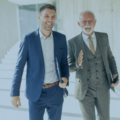 Ein älterer und ein jüngerer Geschäftsmann laufen einen Gang entlang und diskutieren.