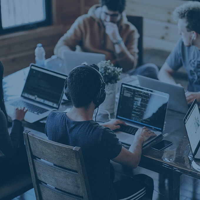 Junge Mitarbeitende eines Startups sitzen an einem Tisch vor ihren Laptops